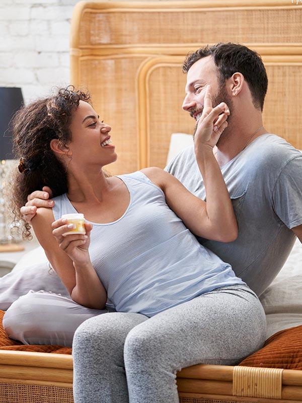 Una pareja sentada en una cama y sonriéndose