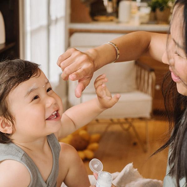 Mãe a pôr creme Mustela no rosto do seu filho