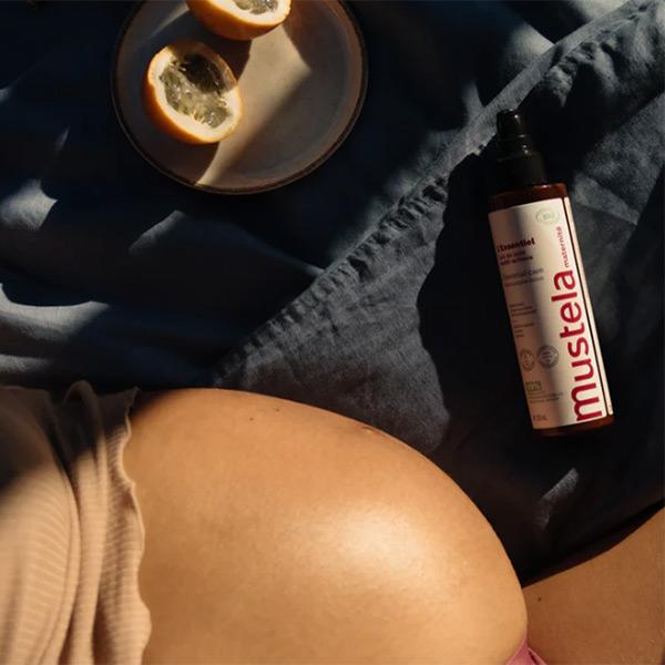 A pregnant woman sitting in bed rubs cream on her belly