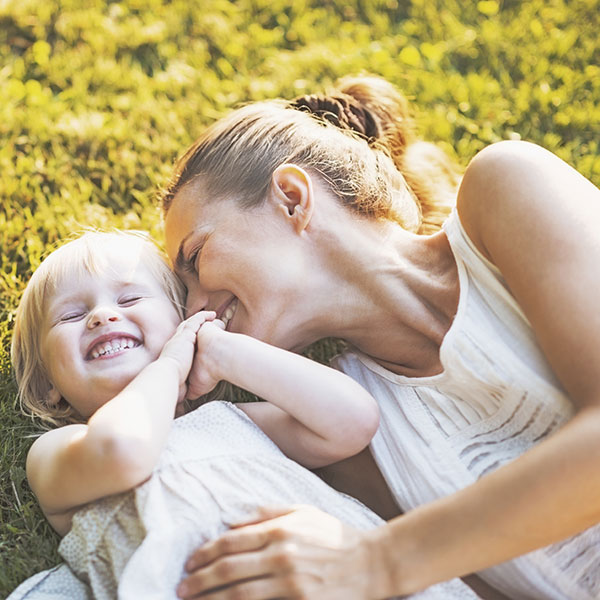 Une maman fait un calin à sa fille allongées dans l'herbe